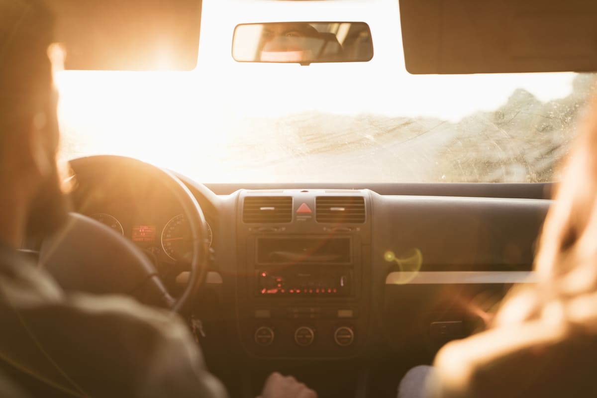 Casal viaja de carro sob sol forte, destacando os cuidados com o carro no verão.