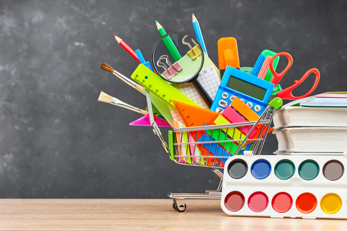 Carrinho em miniatura com tesoura, caneta, lápis, pincéis entre outros materiais em diversas cores, representando como economizar no material escolar.