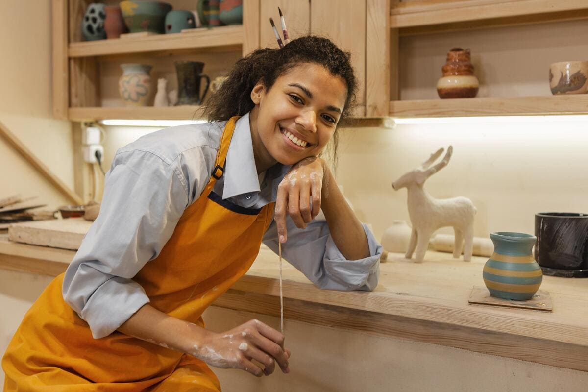 Jovem artesã sorridente em seu ateliê de cerâmica, uma das formas criativas de como ganhar dinheiro em casa com a venda de produtos artesanais.
