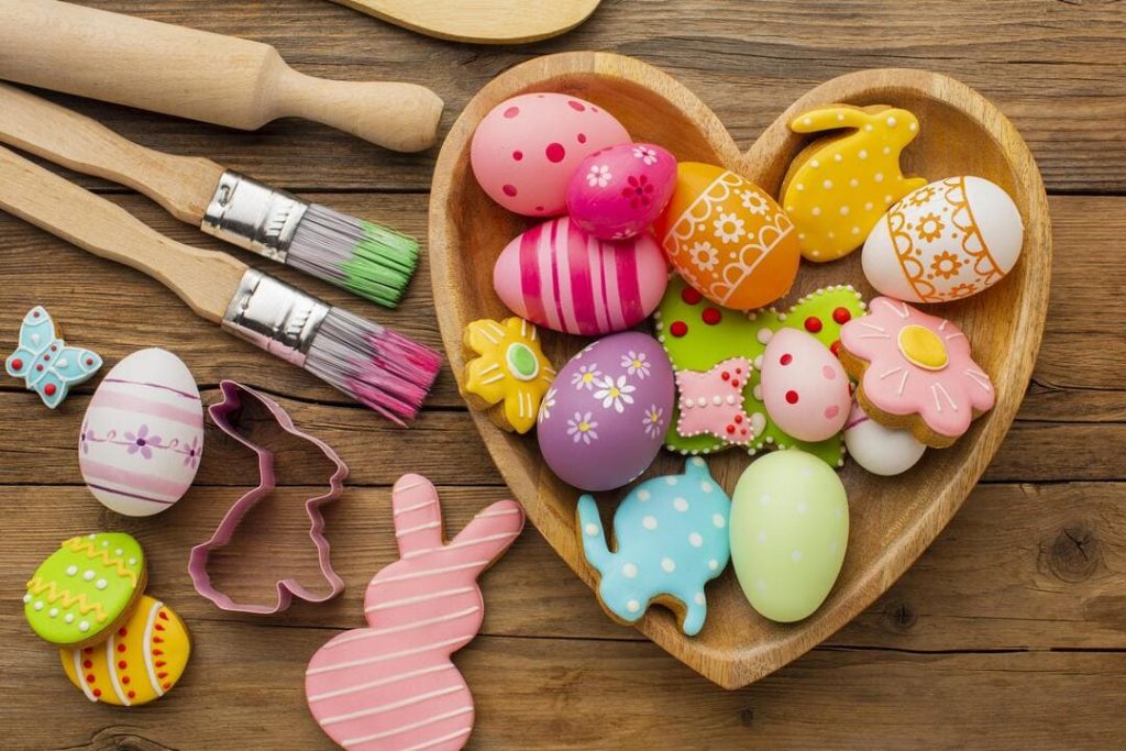 Páscoa para empreender: uma vasilha de madeira em formato de coração, cheia de ovos coloridos e biscoitos decorados. 