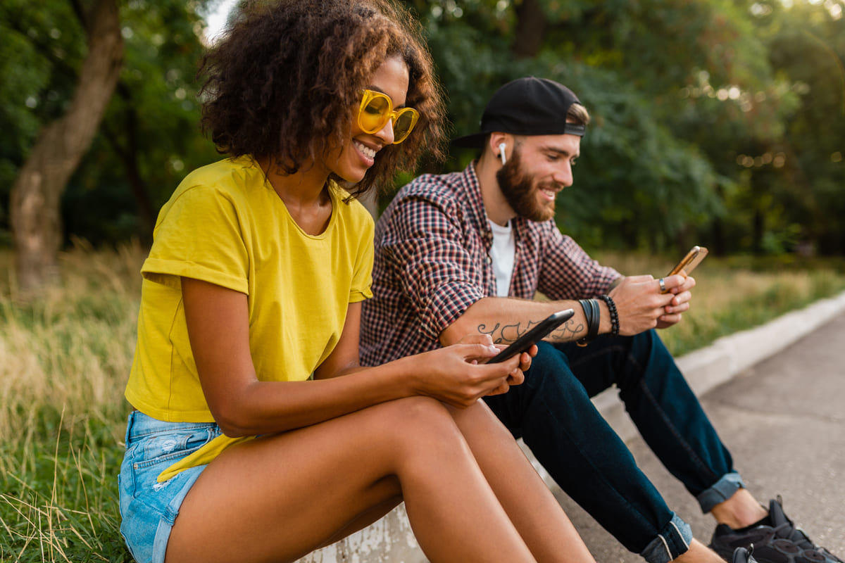 Jovens usando celular ao ar livre para pesquisar sobre consórcio iPhone.