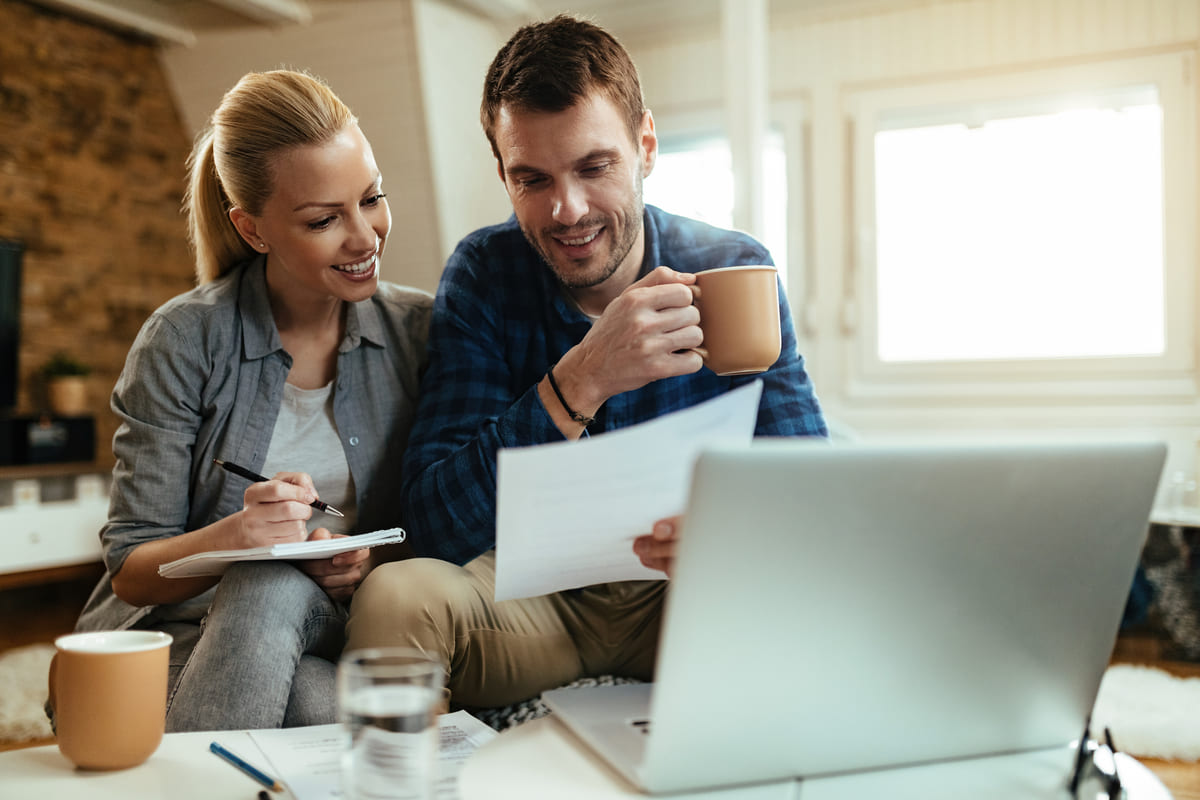 Casal sorri ao analisar documentos e notebook para planejar a estabilidade financeira.