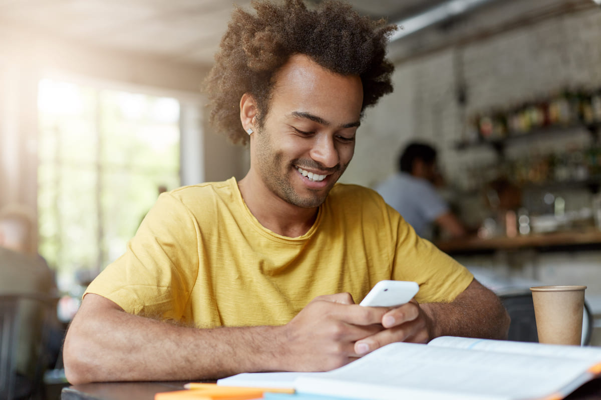 Homem sorri ao usar o celular na mesa para aprender como ganhar pontos Livelo.