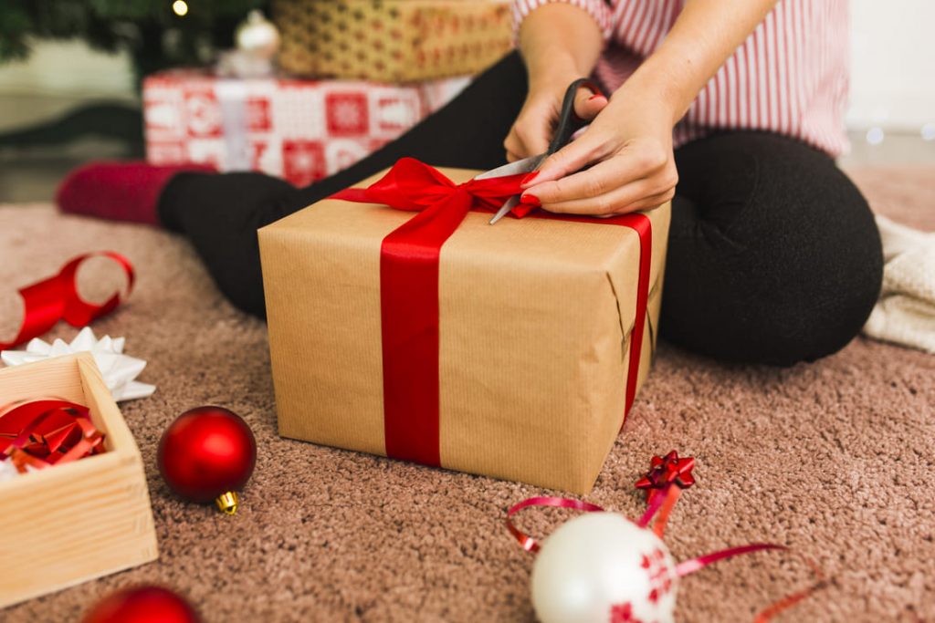 presentes de natal criativos: uma pessoa finalizando um embrulho de presente de natal, com uma fita vermelha.