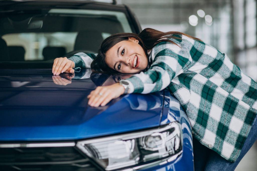carro novo: uma mulher feliz deitada de lado em cima do carro na cor azul metálica.