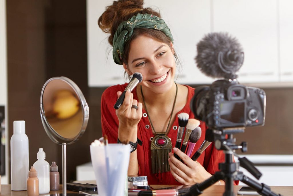 serviços de beleza: mulher de blusa vermelha filmando vídeo de maquiagem.