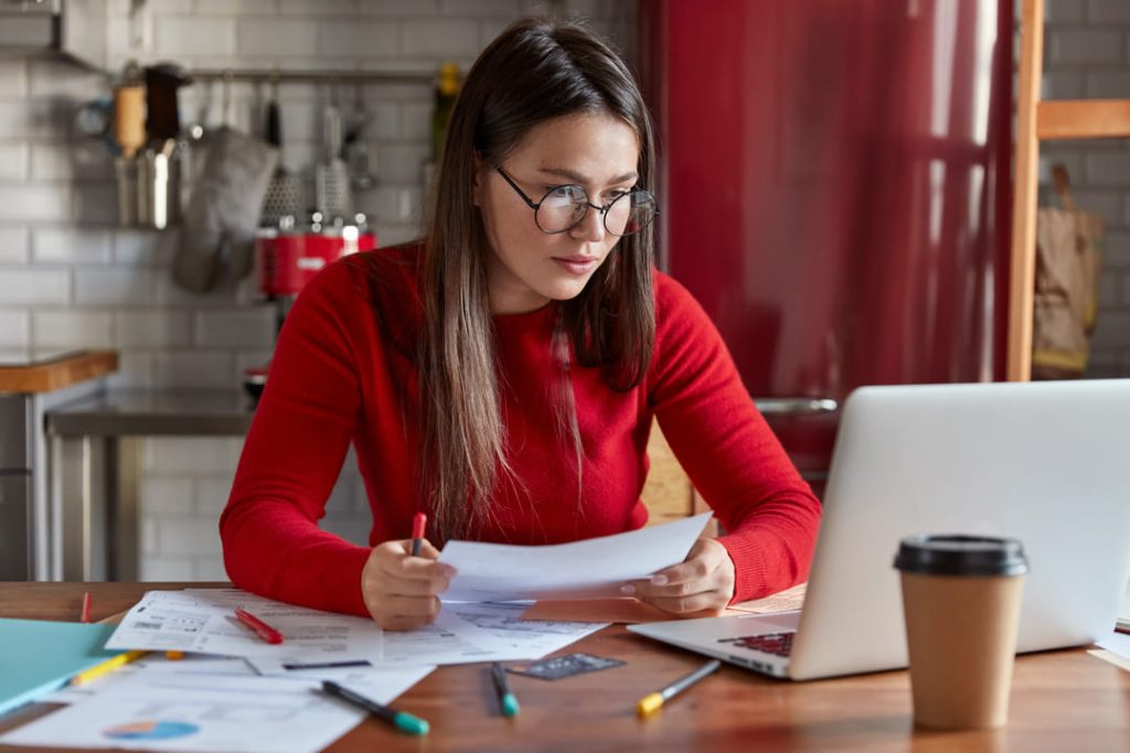 O que é a regra 70/30: uma mulher de blusa vermelha, analisando as contas e olhando no notebook. 