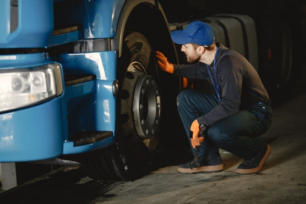 Manutenção de caminhões: um mecânico abaixado inspecionando a roda de um caminhão.