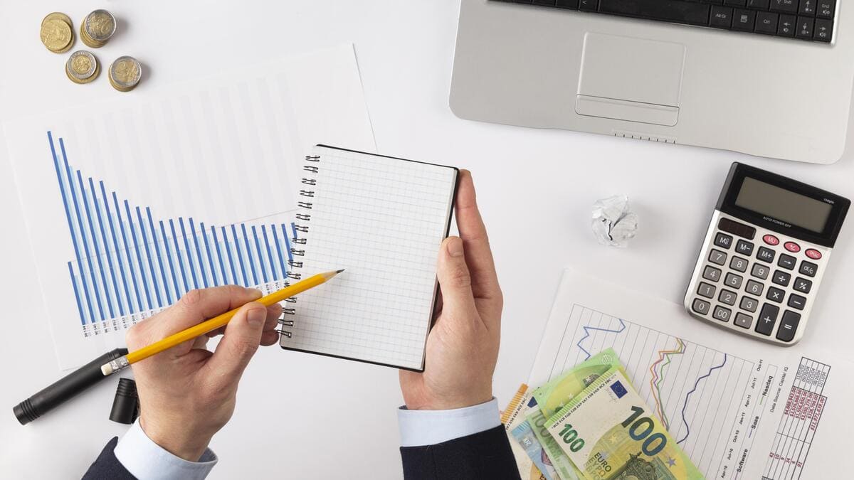 Executivo escrevendo em agenda e calculadora para organizar o calendário financeiro.