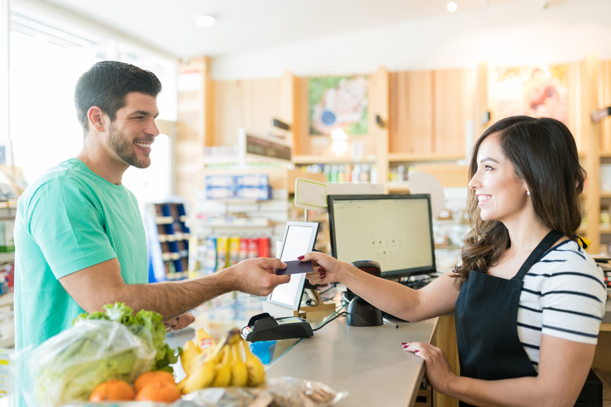 Homem sorrindo para lojista na hora de pagar suas compras e após ter solicitado o pagamento com cartão de crédito ou débito.