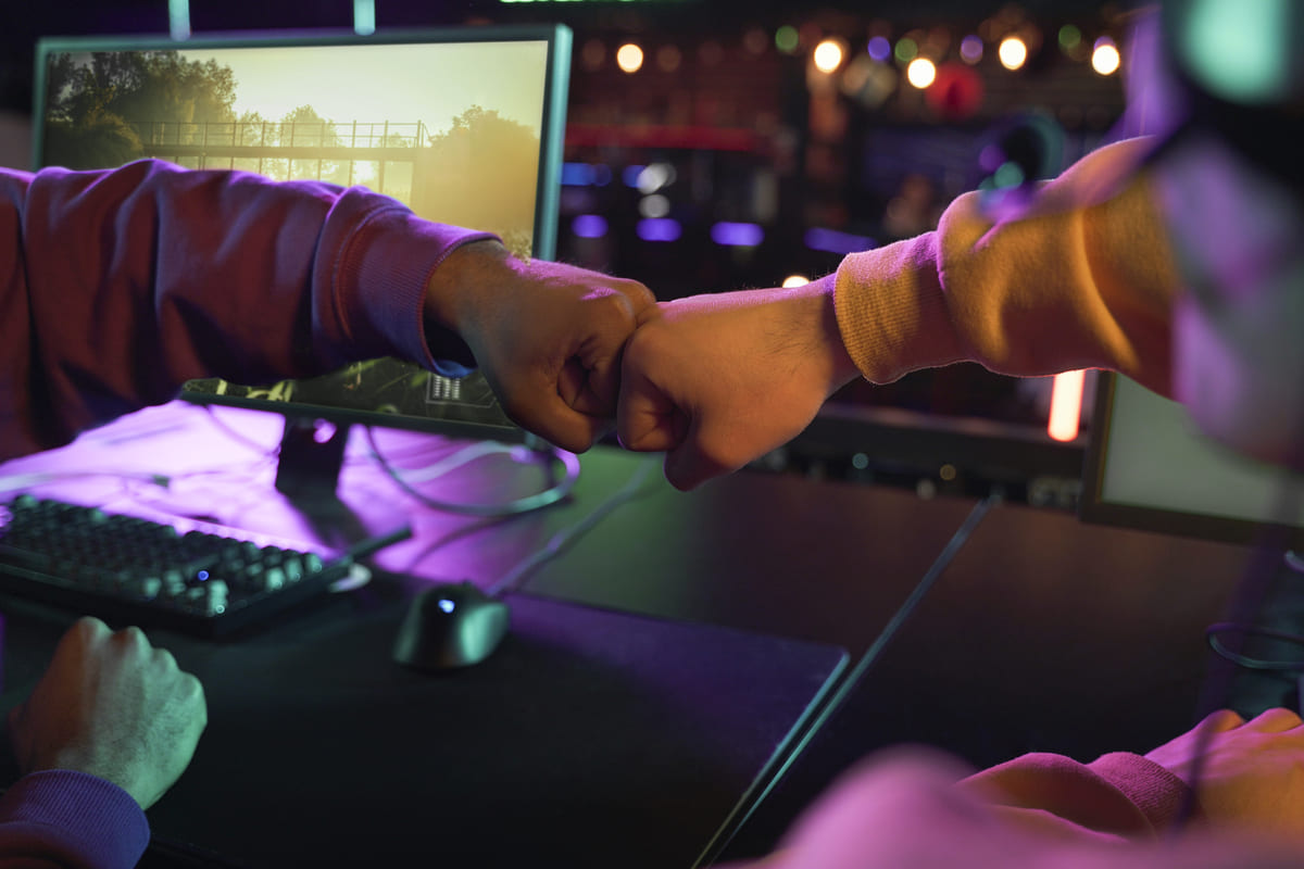 Dois punhos se tocando com telas exibindo jogos ao fundo, representando o cenário competitivo e o que são e-sports.