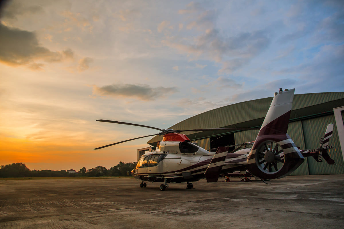 Helicóptero estacionado em frente ao hangar durante o pôr do sol, representando opções de investimento em consórcio de aeronaves.