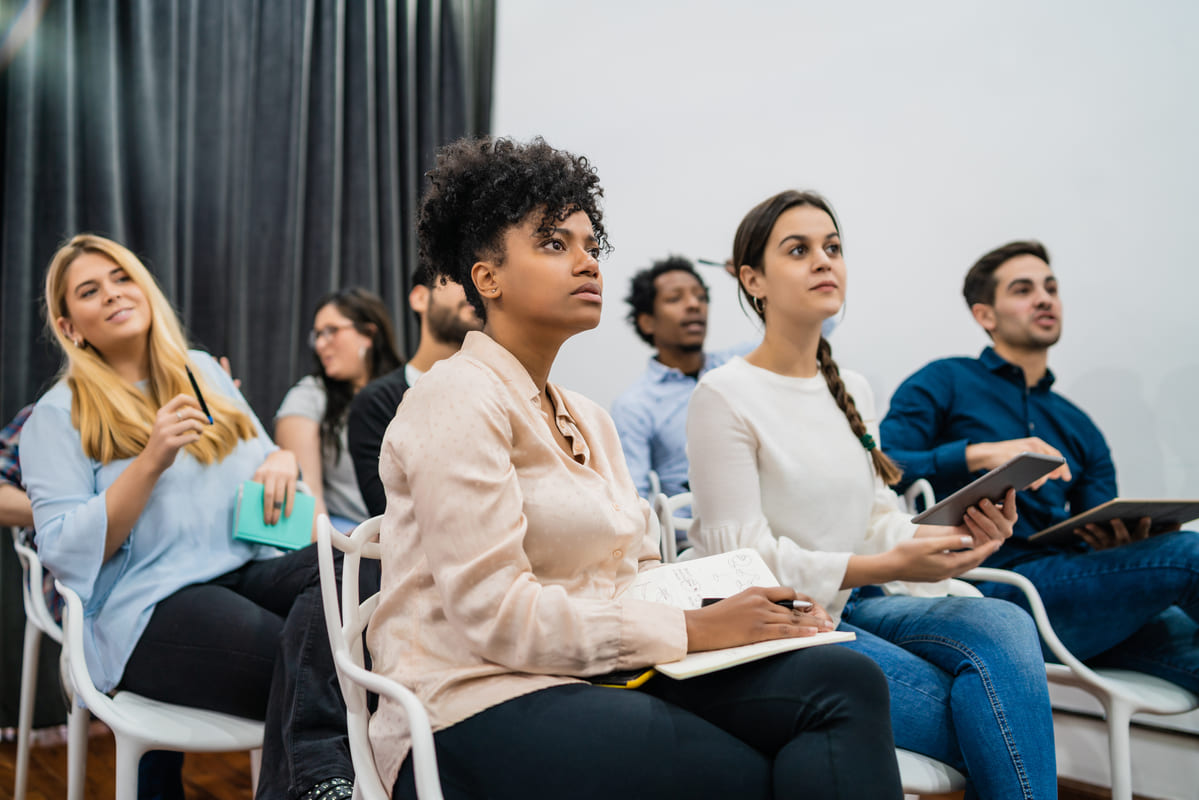 Grupo de pessoas atentas em palestra segura cadernos e tablets, buscando entender os termos técnicos do glossário do consórcio.