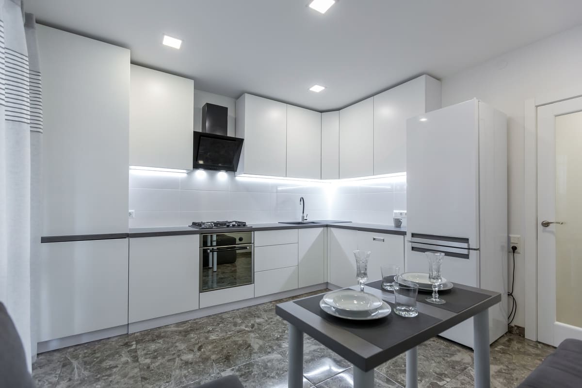 Ambiente com armários brancos, iluminação embutida e mesa de jantar, ilustrando o design prático e otimizado de uma cozinha modulada.