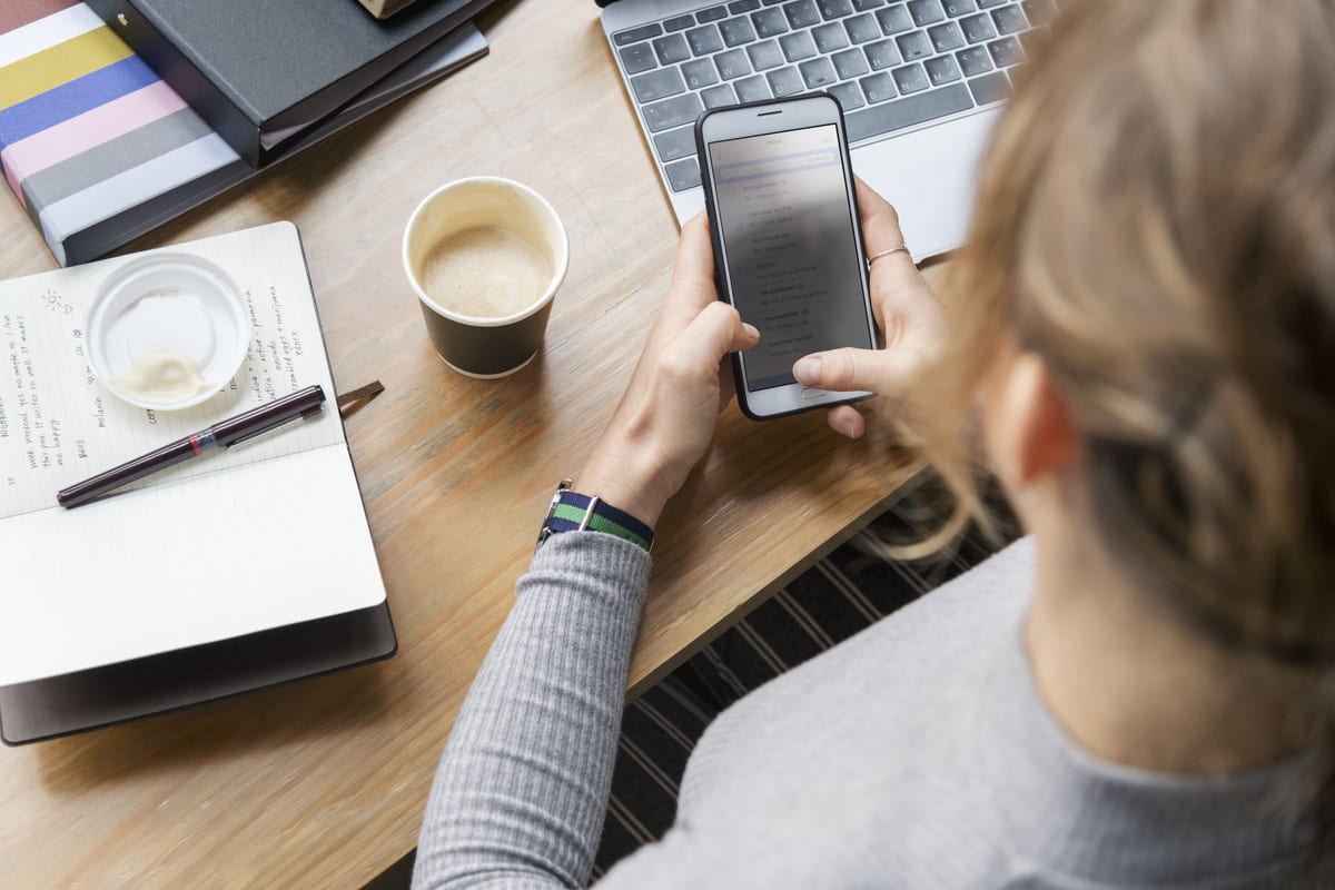 Mulher utiliza smartphone em sua mesa de trabalho enquanto pesquisa como comprar celular sem cartão de crédito.