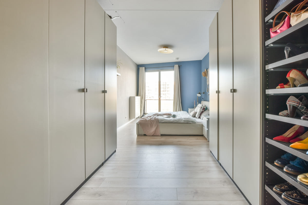 O resultado de como fazer um closet dentro do quarto ilustrado por um corredor de armários altos fechados que dá acesso direto à cama e à janela ao fundo.