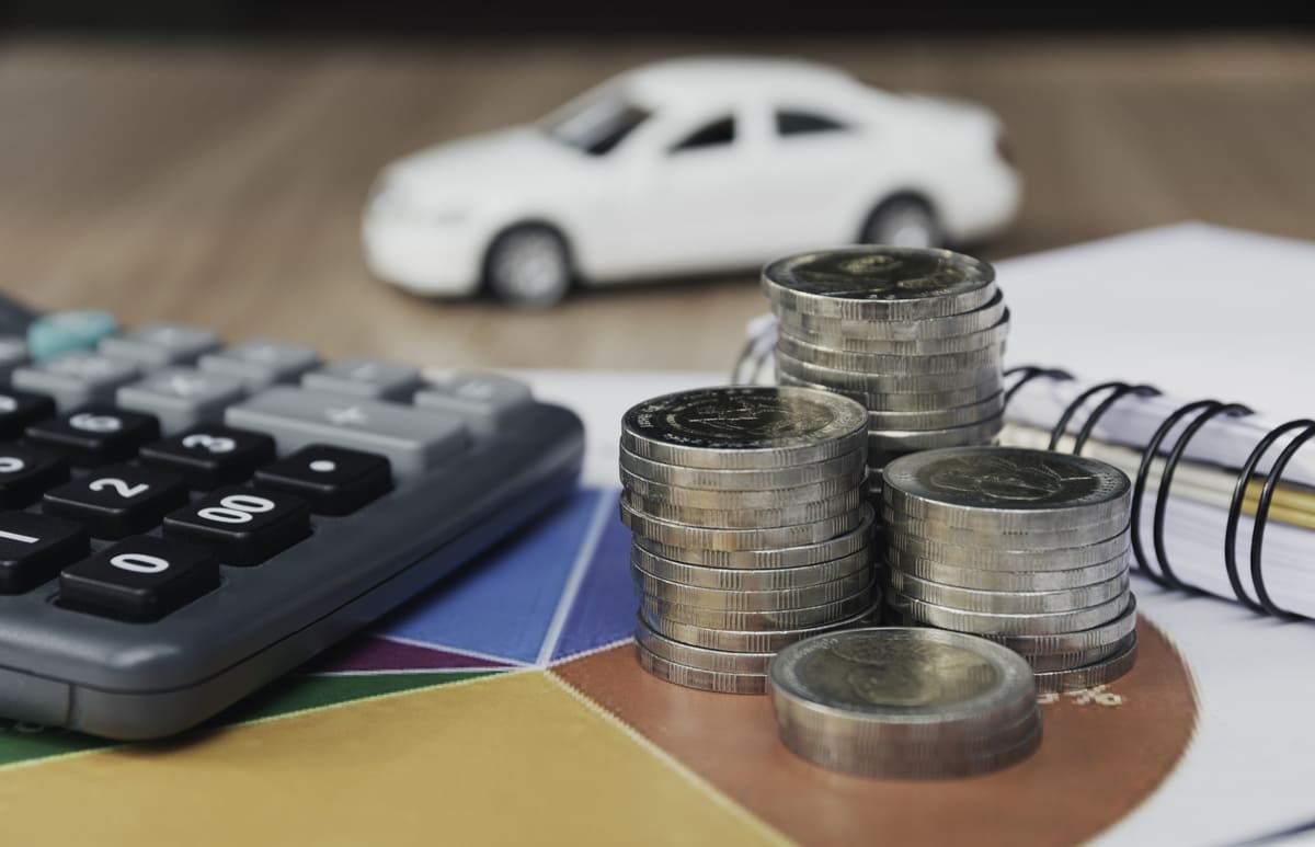 O impacto do IPI nos automóveis é demonstrado por pilhas de moedas e uma calculadora sobre um gráfico colorido com um carro branco desfocado ao fundo.