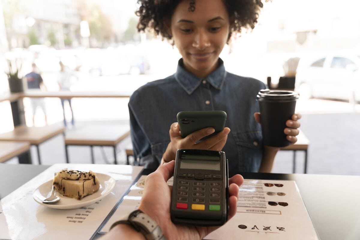 Cliente aproxima o smartphone da maquininha para pagar a conta do café por aproximação, mostrando a praticidade do cartão virtual.