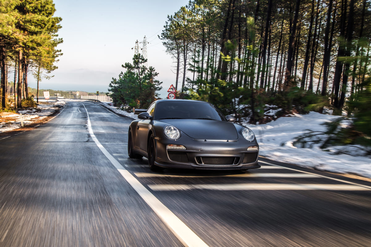 Porsche esportivo cinza fosco em movimento em estrada com neve, destaque entre carros de luxo.