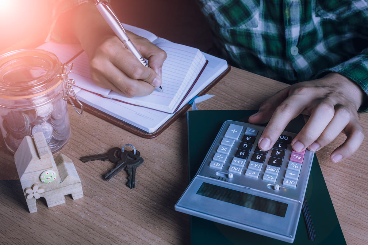 Mãos usam calculadora e caderno para calcular a taxa de adesão de consórcio.