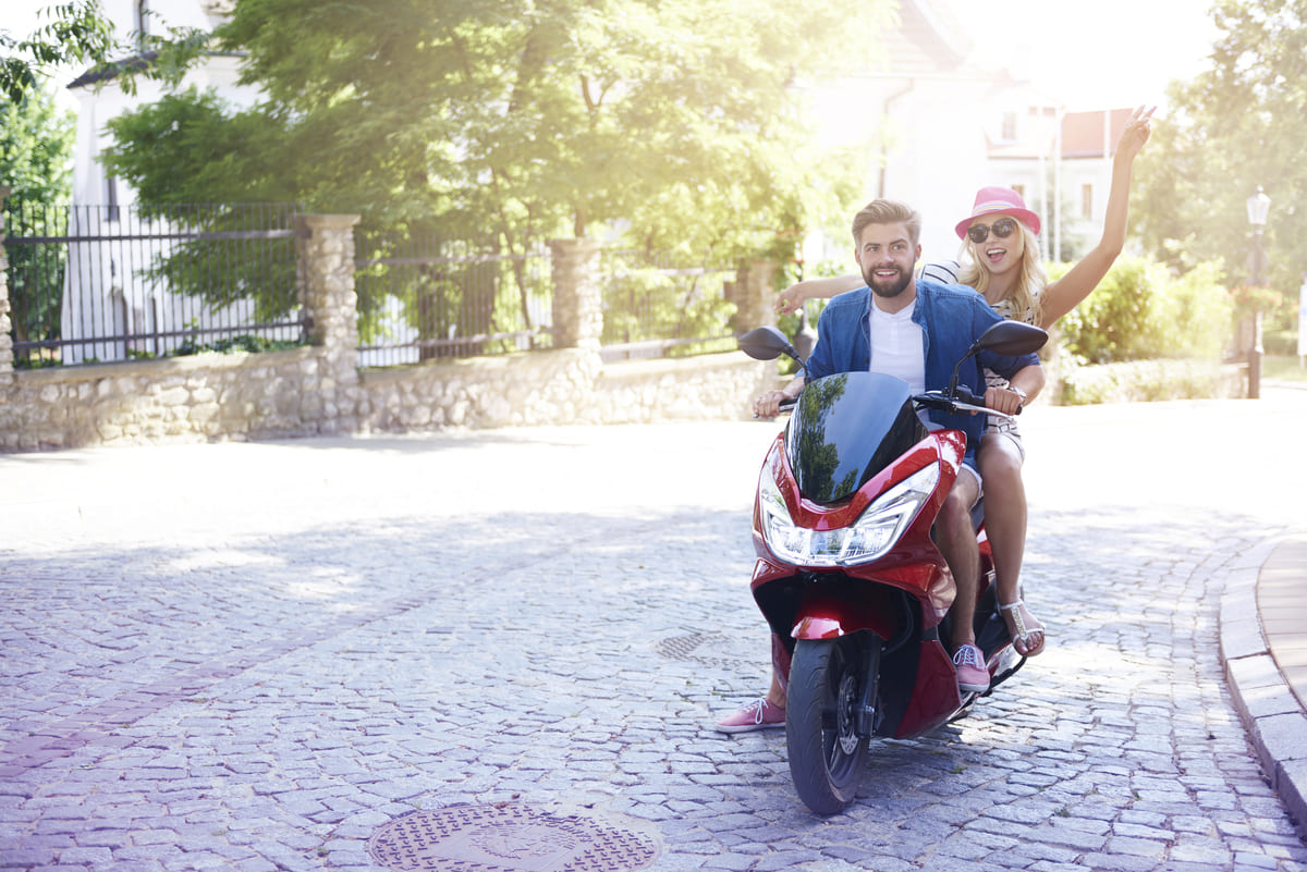 Homem de capacete pilotando uma moto cub vermelha ao ar livre.