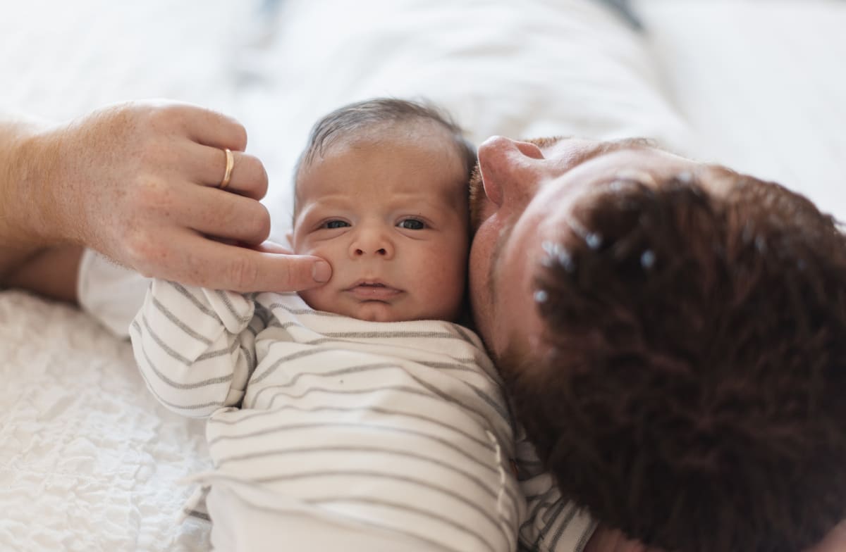 Pai deitado ao lado do bebê recém-nascido celebrando o primeiro dia dos pais.
