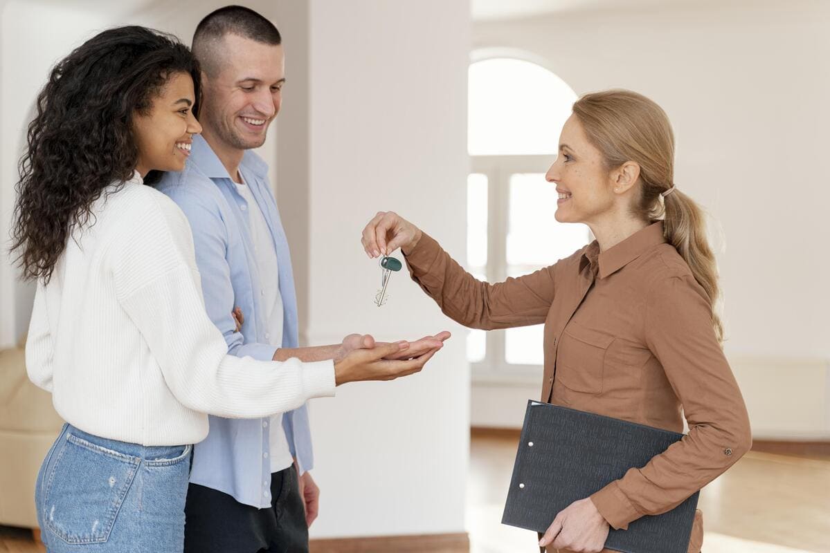 Corretora a entregar chaves a um casal, ilustrando os ciclos do mercado imobiliário.