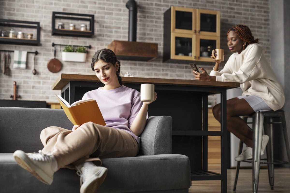 Duas pessoas compartilhando espaço de co-living enquanto leem e tomam café.